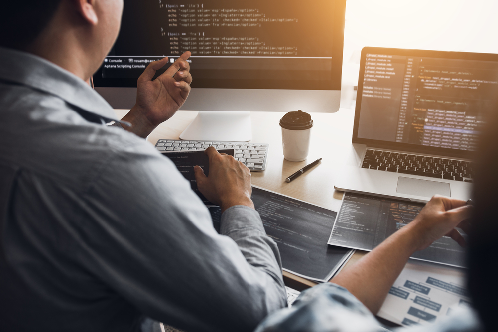 兩名軟件開(kāi)發(fā)人員正在使用計(jì)算機(jī)與辦公桌上的合作伙伴一起工作